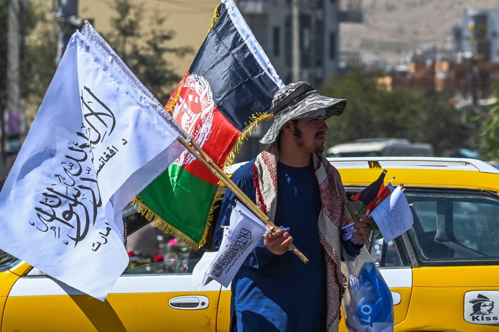 بائع متجول أفغاني يحمل أعلام أفغانستان الوطنية وأعلام طالبان لبيعها عند تقاطع شارع في كابول.أ.ف.ب