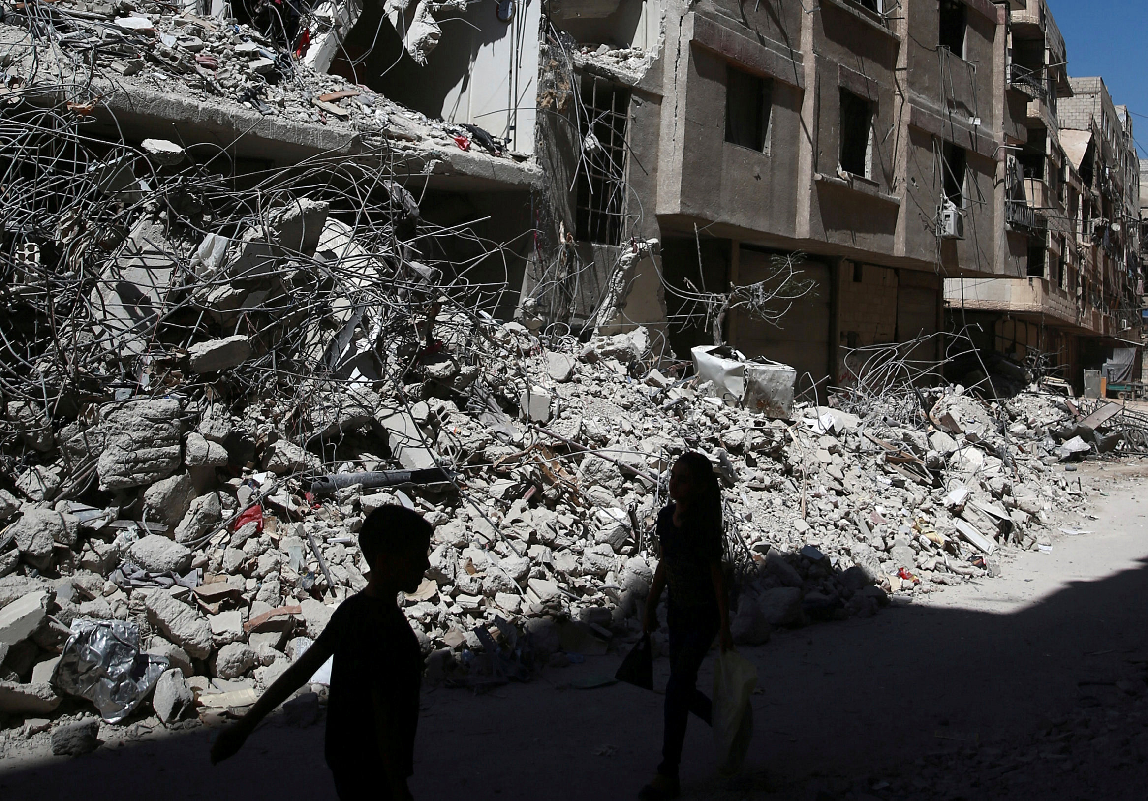 FILE PHOTO: Children walk past rubble of damaged buildings at Ain Tarma, eastern Damascus suburb of Ghouta