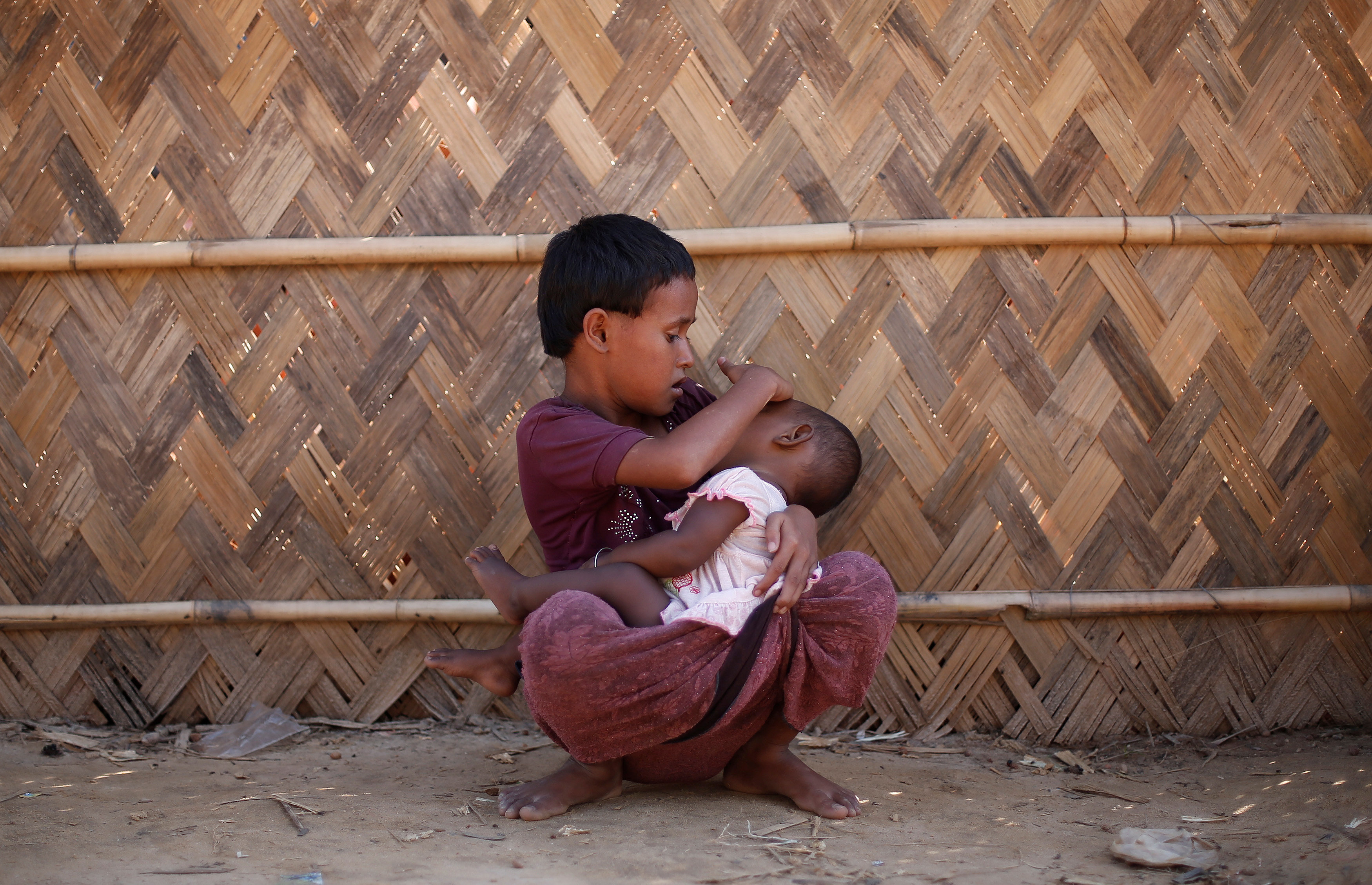 A Rohingya refugee girl holds her sister as she sits outside a medical center at a refugee camp in Palong Khali