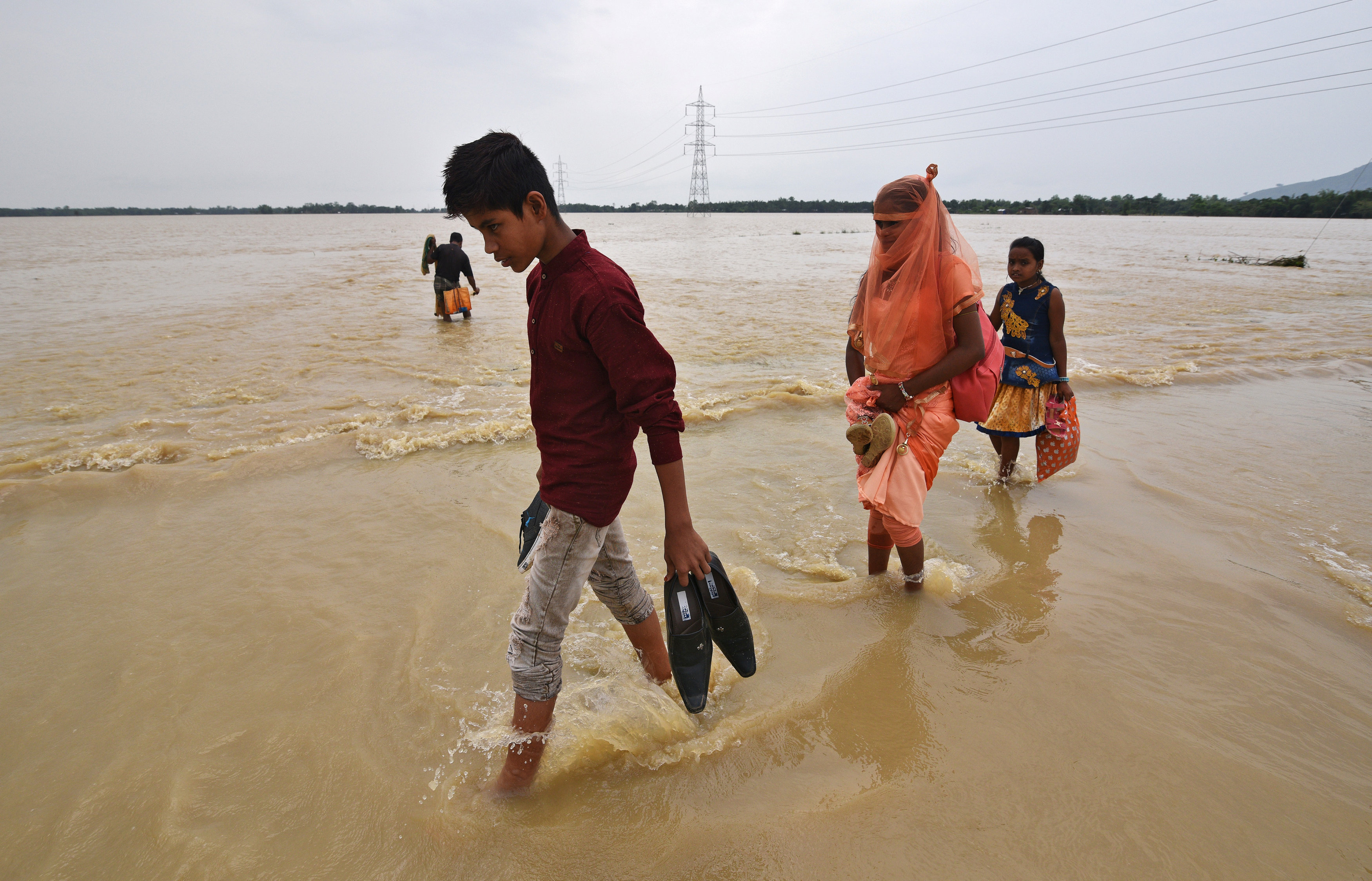 Villagers wade through a flooded road near a village in Hojai