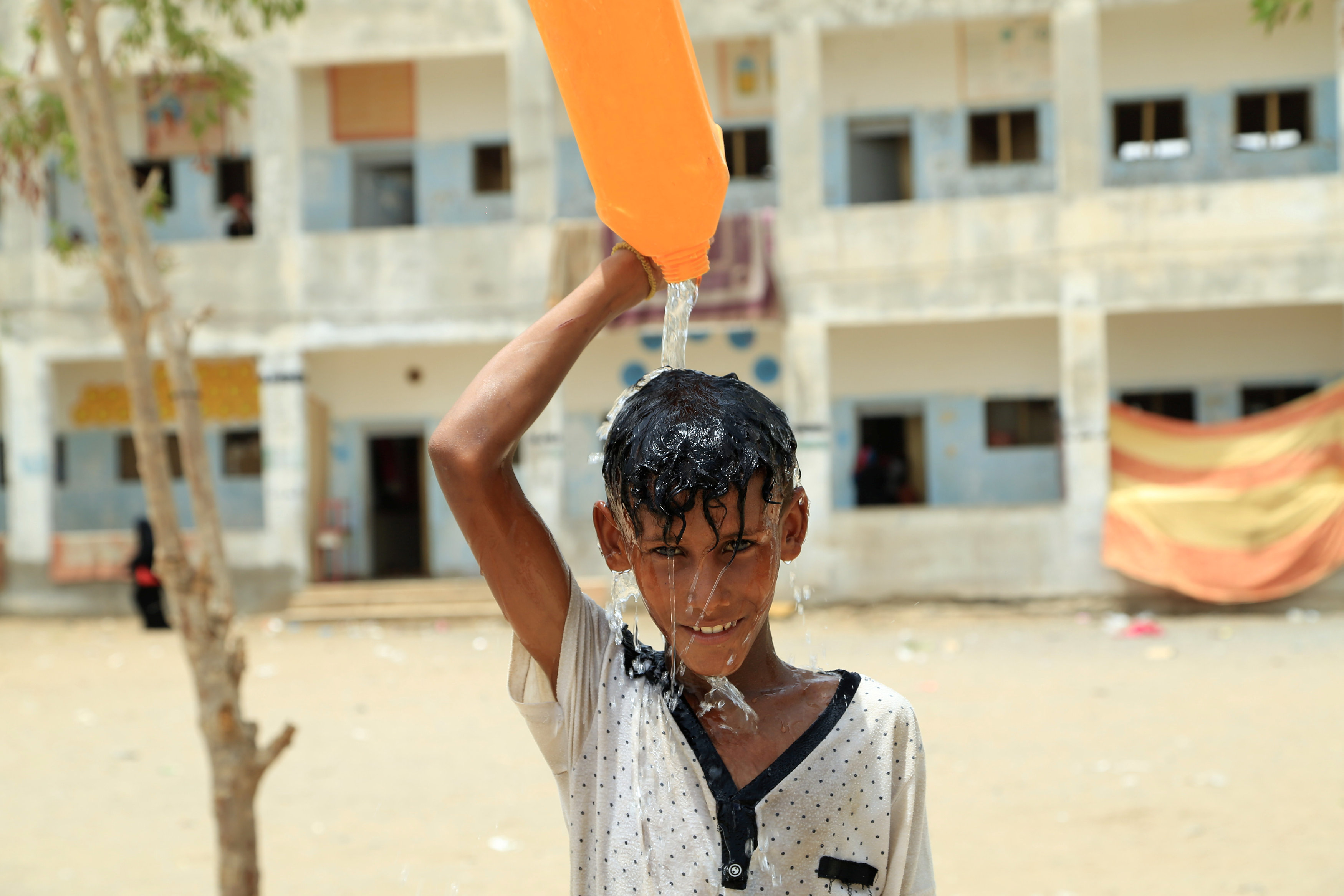Displaced boy pours water on his head in al-Marawia