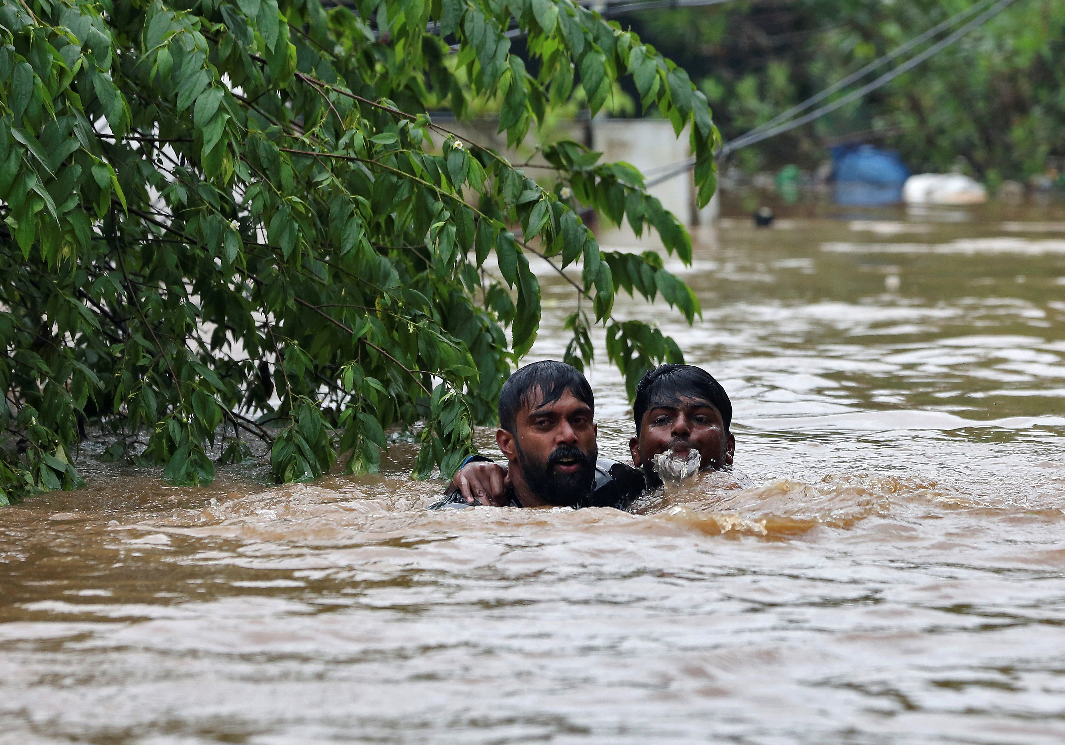 A man rescues a drowning man from a flooded area after the opening of Idamalayr, Cheruthoni and Mullaperiyar dam shutters following heavy rains, on the outskirts of Kochi