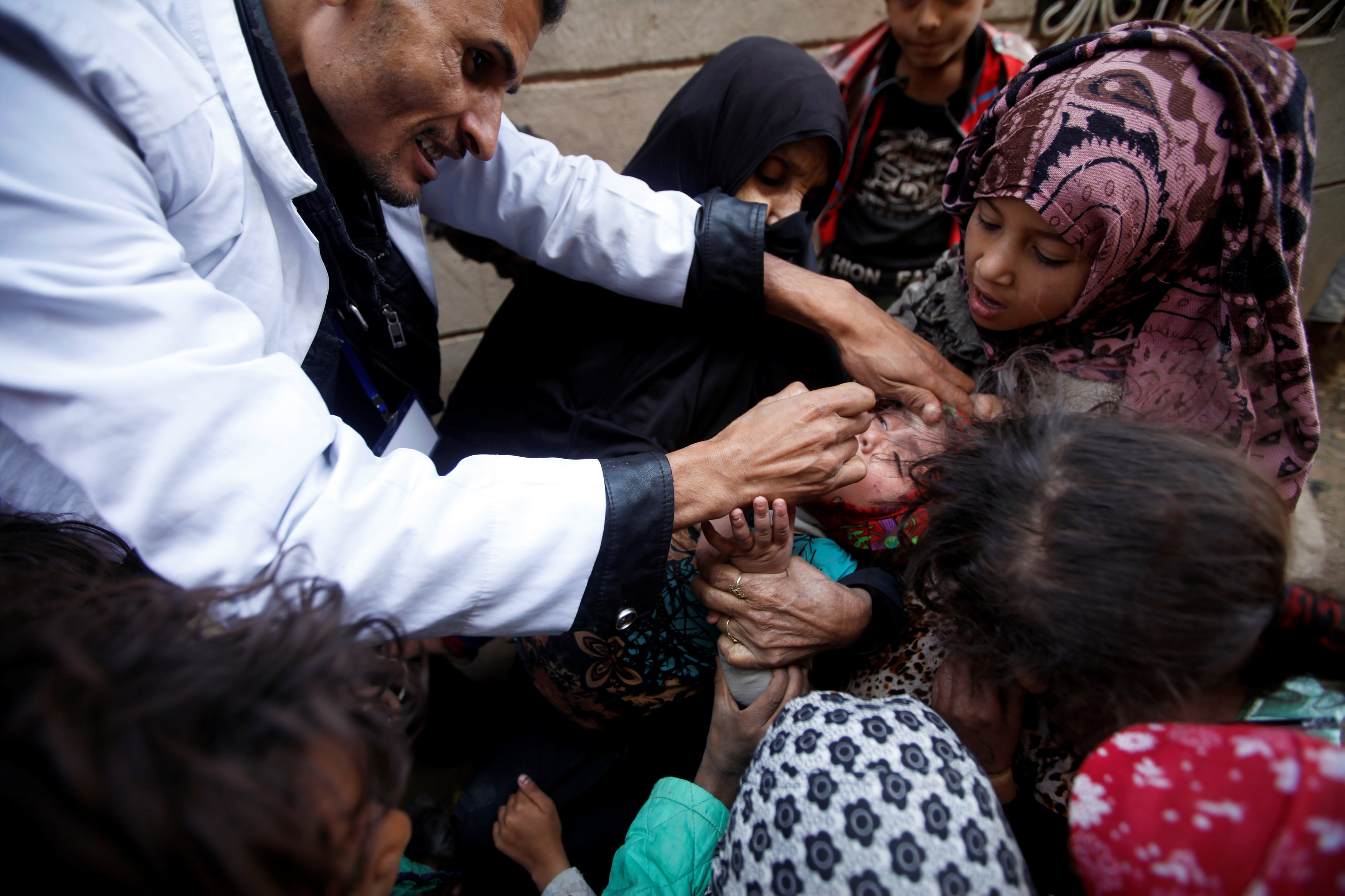 Children gather around a girl receiving a polio vaccination during a house-to-house polio immunisation campaign in Sanaa