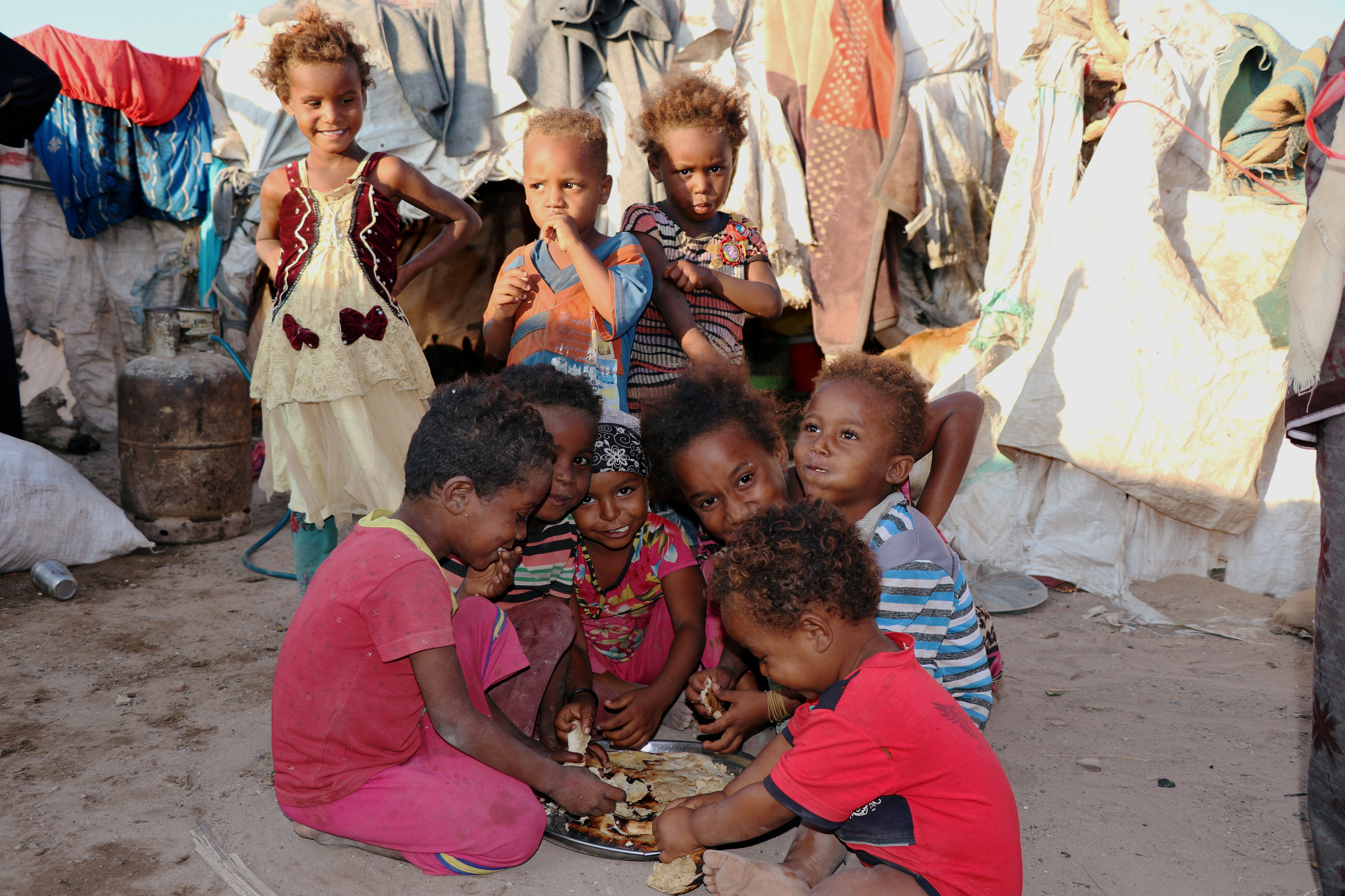 Children eat bread at a camp sheltering displaced people from the Red Sea port city of Hodeidah near Aden, Yemen