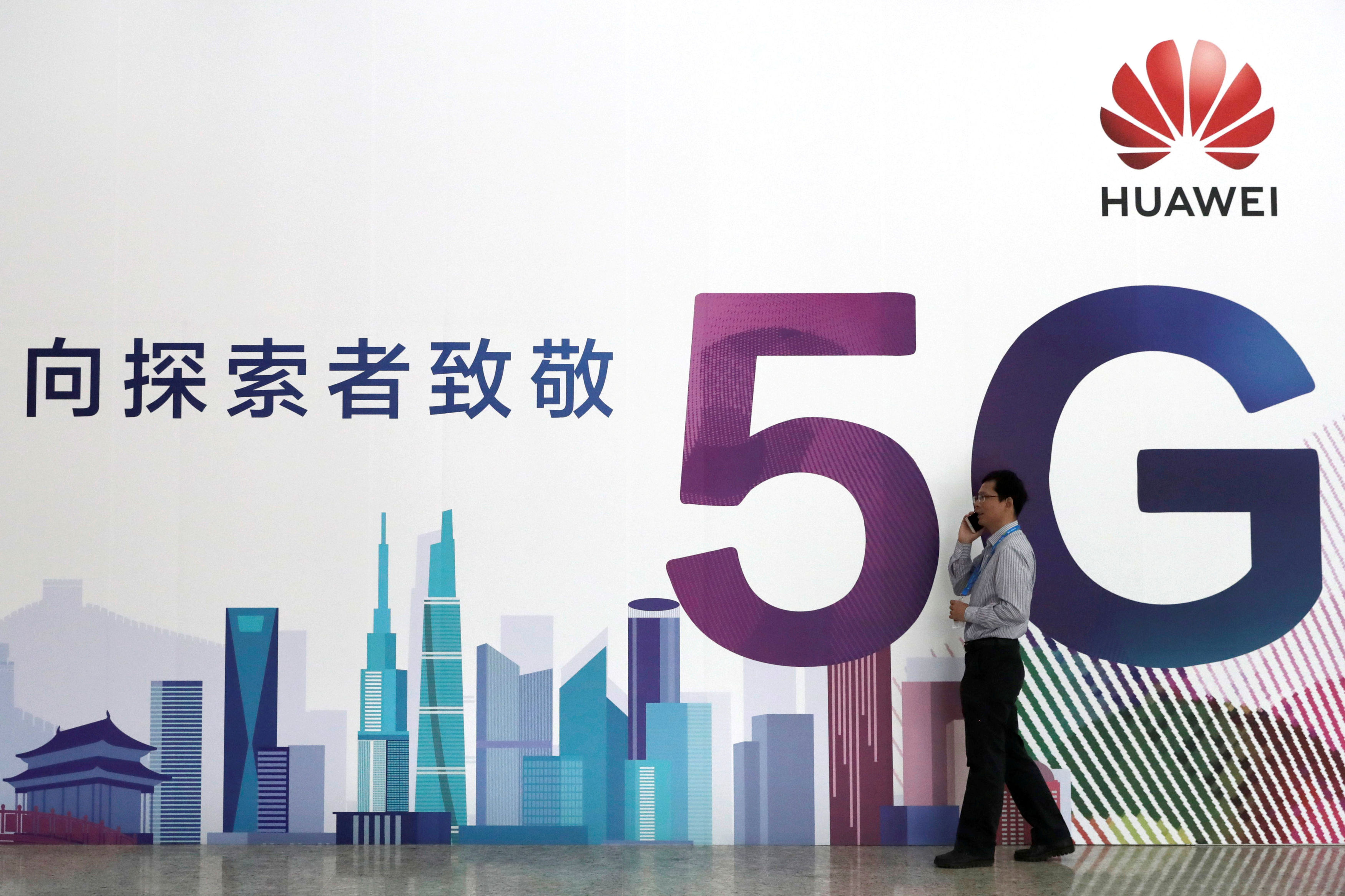 FILE PHOTO: A man talks on his mobile phone beside Huawei's billboard featuring 5G technology at the PT Expo in Beijing