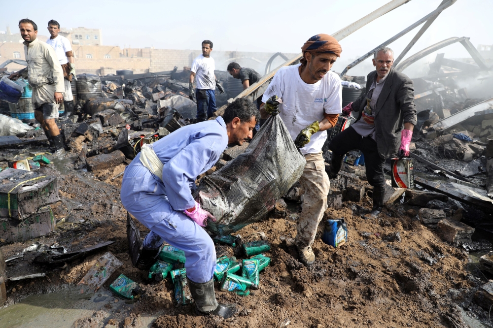 Workers salvage a sack containing oil canisters from the wreckage of a vehicle oil and tires store hit by Saudi-led air strikes in Sanaa