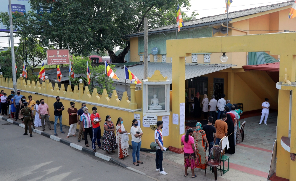 People wearing protective masks wait in a line outside a polling station as they prepare to cast their vote during the country's parliamentary election in Colombo