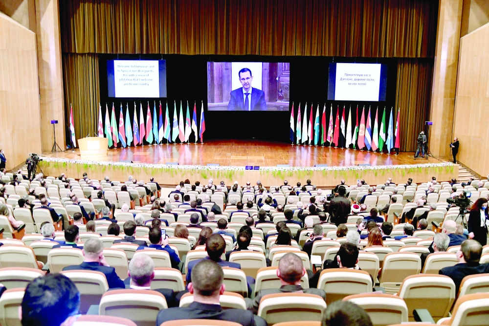 Syria's President Bashar al-Assad is seen on screen as he speaks during the international conference on the return of Syrian refugees in Damascus