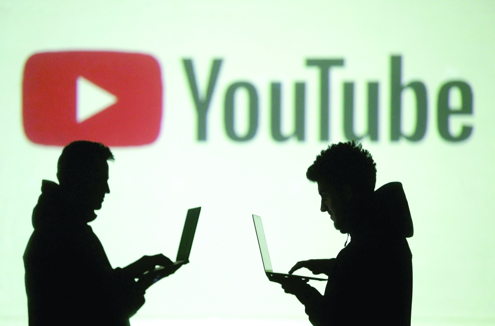 Silhouettes of mobile device users are seen next to a screen projection of Youtube logo in this picture illustration