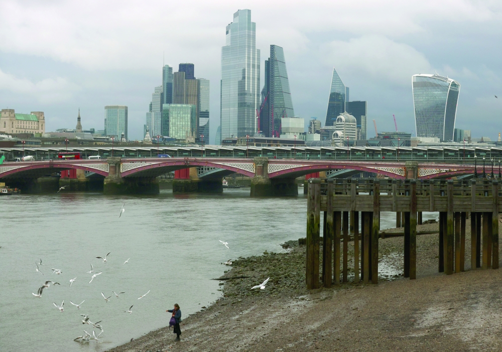 A woman feeds birds on the bank of the river Thames with London's financial district seen in the background, amid the coronavirus disease (COVID-19) in London