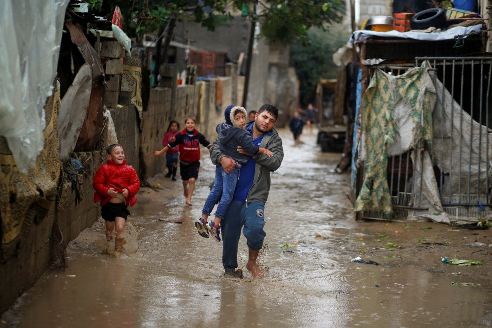 A Palestinian man carries his brother as he walks through flood waters following heavy rains in the northern Gaza Strip
