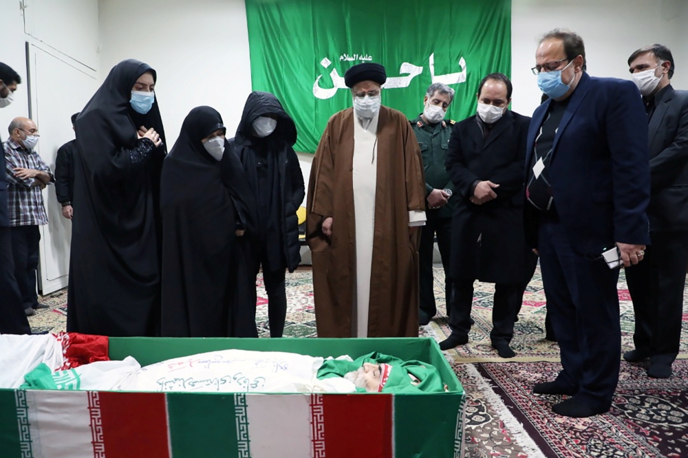 Ebrahim Raisi, head of Iran's judiciary, and family members of Iranian nuclear scientist Mohsen Fakhrizadeh, stand next to his body in Tehran